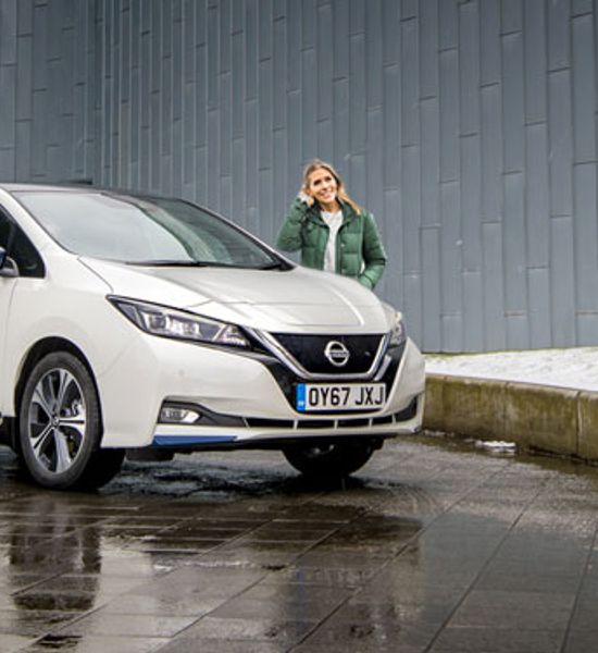 Nicki Shields standing behind a white Nissan Leaf in the rain