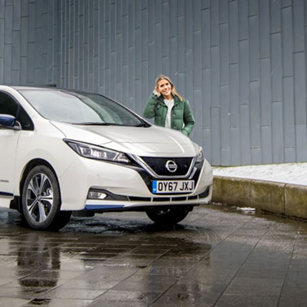 Nicki Shields standing behind a white Nissan Leaf in the rain
