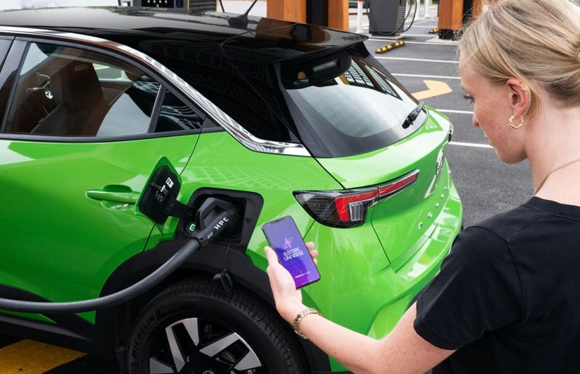 Green Vauxhall Mokka plugged into rapid charger with Octopus Energy app showing on phone held by young lady